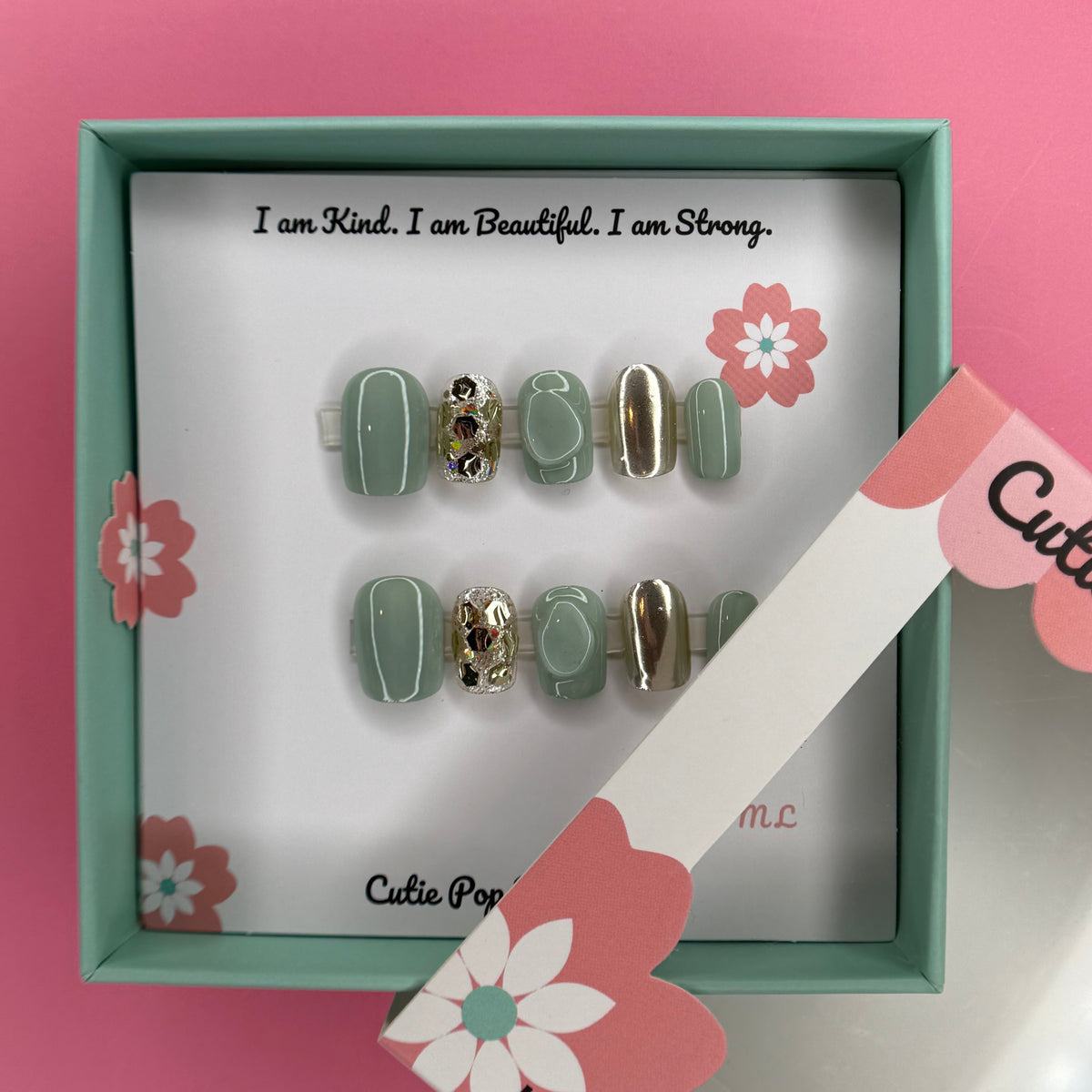 Green and gold sparkle press-on nails by Cutie Pop Nail Shop, showcasing shiny, decorative nail tips with a glittery finish.