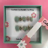 Green and gold sparkle press-on nails by Cutie Pop Nail Shop, showcasing shiny, decorative nail tips with a glittery finish.