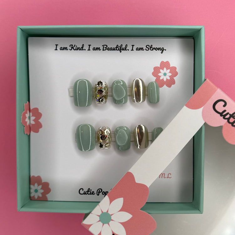Green and gold sparkle press-on nails by Cutie Pop Nail Shop, showcasing shiny, decorative nail tips with a glittery finish.