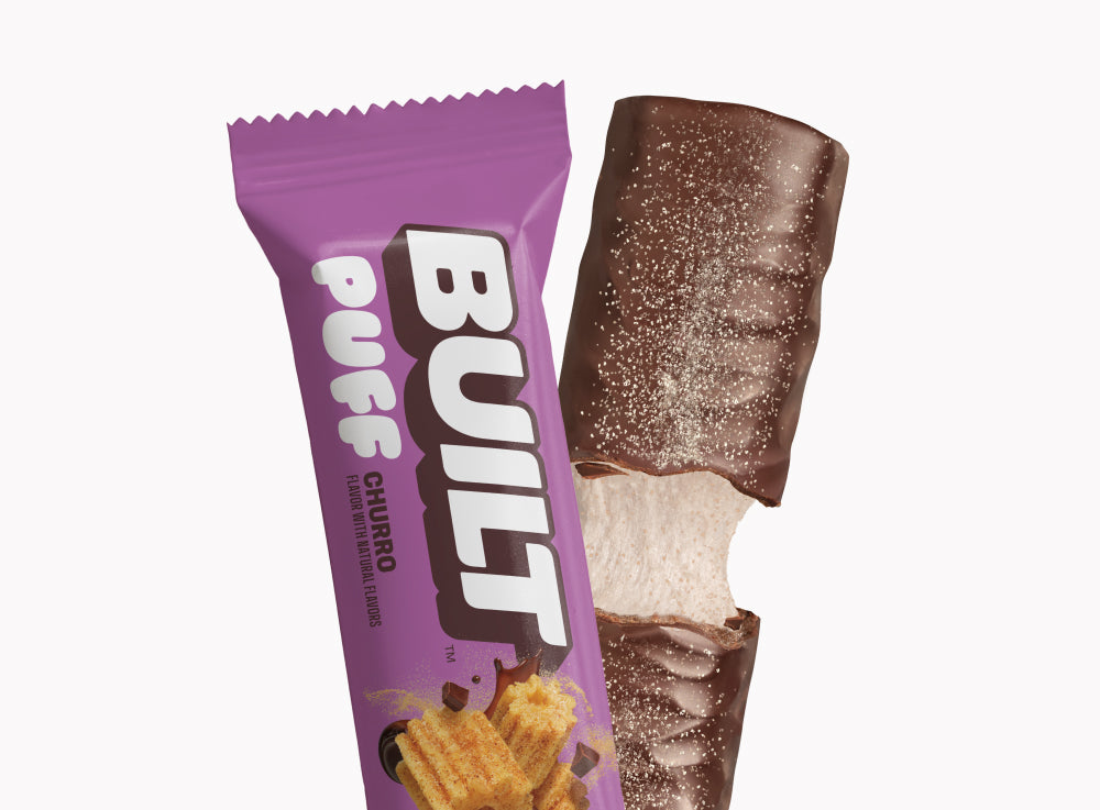 BUILT Churro Puff snack with crispy churro-flavored exterior and soft filling, displayed on a grid background.