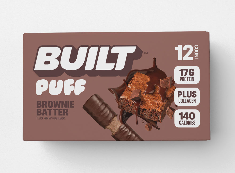 BUILT Brownie Batter Puff stacked inside a carton, showcasing the soft, chocolate-flavored snack with a brown puff exterior.