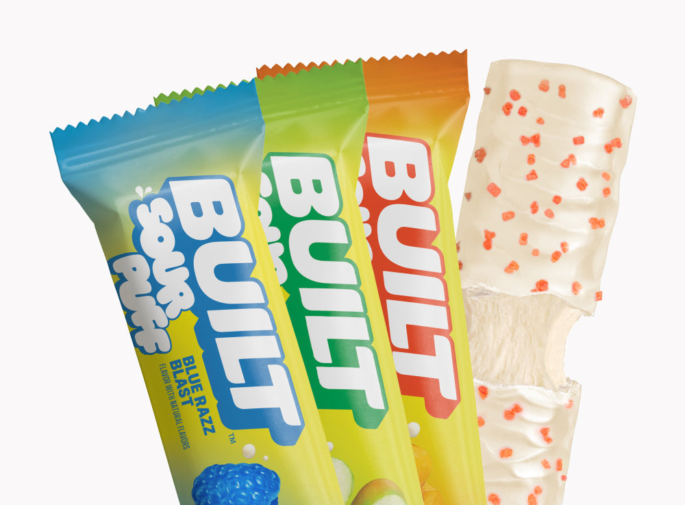 Assorted BUILT Sour Puffs in a 12-count variety box, colorful chewy sour candies with fruity flavors on a grid background.