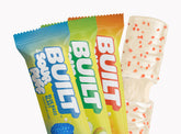 Assorted BUILT Sour Puffs in a 12-count variety box, colorful chewy sour candies with fruity flavors on a grid background.