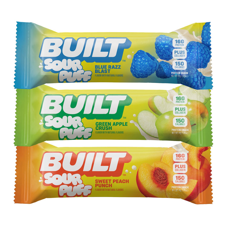 Stack of BUILT Sour Puffs in a variety flavor box, showing colorful puff wrappers and a clear view of the snack packaging.