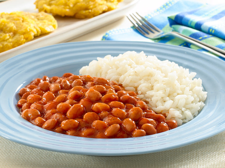 Canned pink beans and rice in a bowl, Goya Habichuelas Rosadas, 15.5 oz, with a spoon and fresh herbs on a plate.