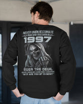 Black T-shirt from TEELUVS.COM with "Never Underestimate Us 1997" printed on the front, displayed on a hanger.