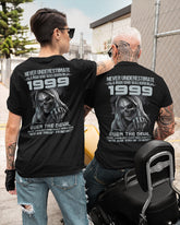 Black TEELUVS.COM T-shirt with "Never Underestimate Us 1999" slogan, displayed flat on a white background.